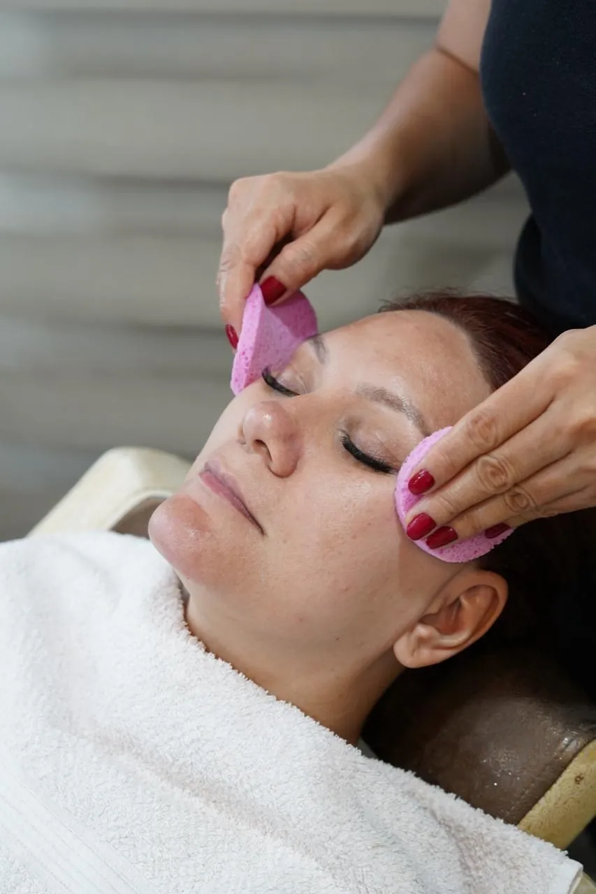 Profesional del salón limpiando el rostro de una clienta con esponjas