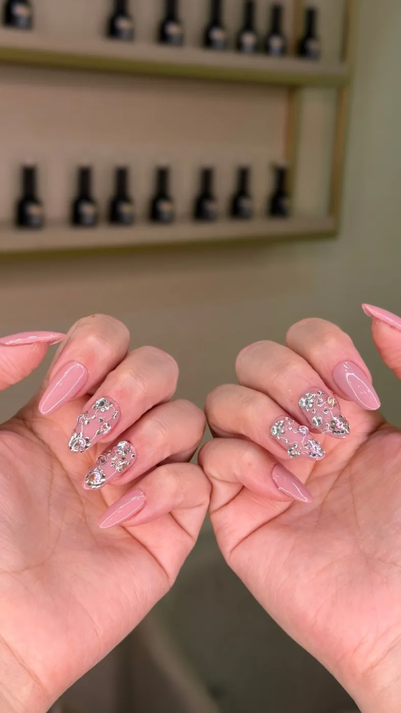 Uñas almendradas rosa con cristales, con los esmaltes del salón de fondo