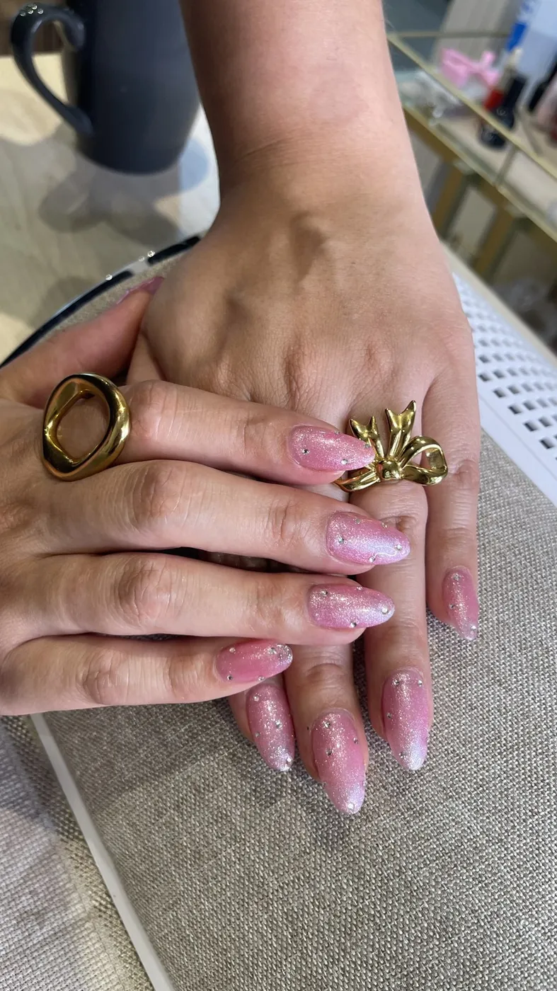 Uñas almendradas con glitter rosa, mano con anillos dorados